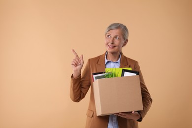 Happy unemployed senior woman with box of personal office belongings on beige background. Space for text