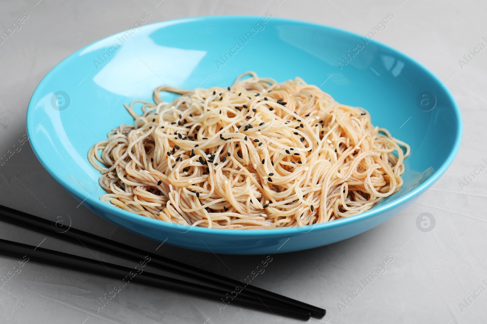 Photo of Plate of noodles with sesame and chopsticks on table, closeup