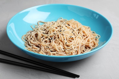 Photo of Plate of noodles with sesame and chopsticks on table, closeup