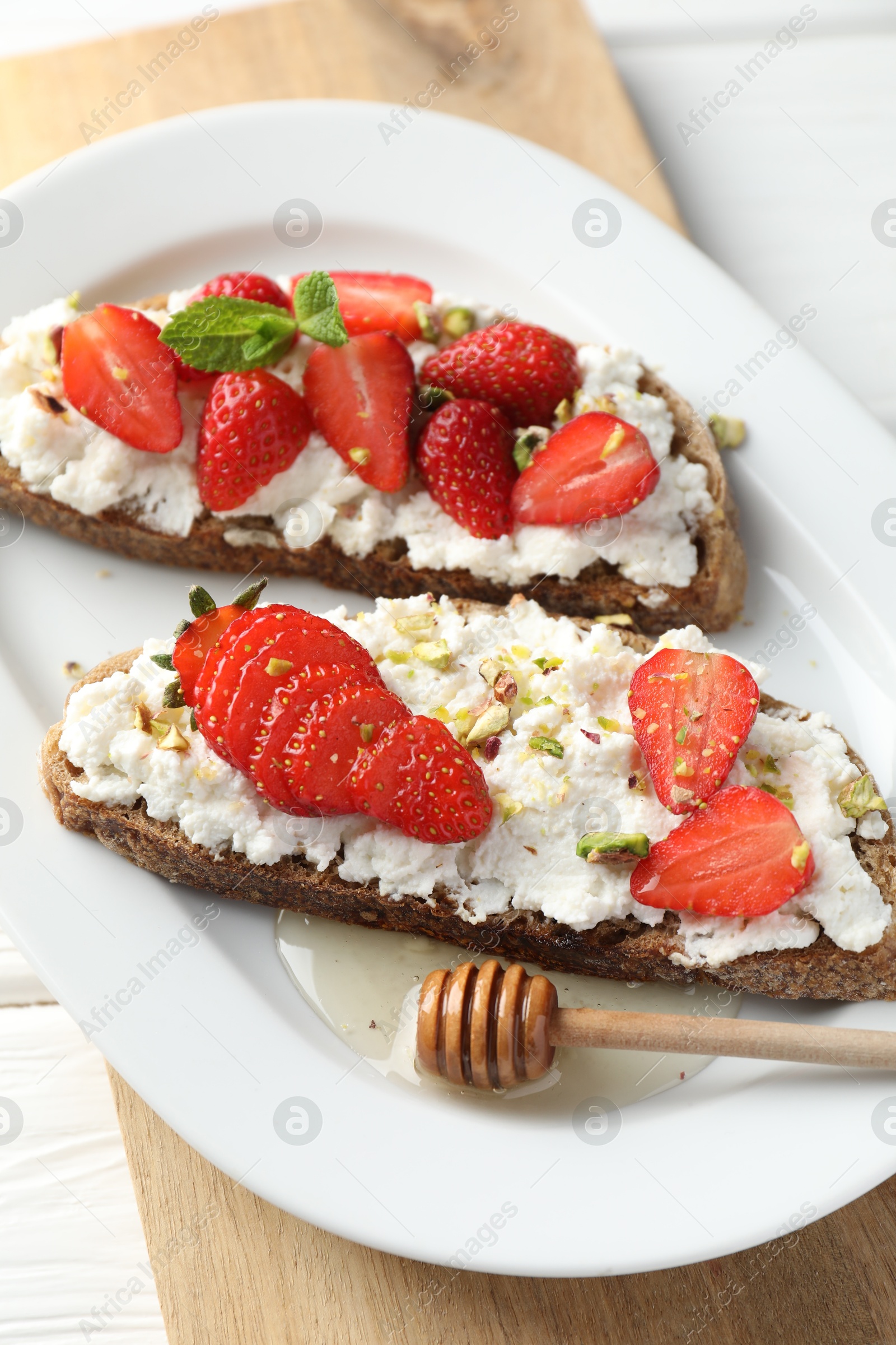 Photo of Delicious ricotta bruschettas with strawberry and pistachios served with honey on white table