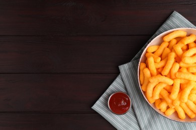 Photo of Crunchy cheesy corn snack in bowl and ketchup on wooden table, flat lay. Space for text