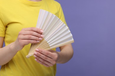 Woman with hand fan on violet background, closeup. Space for text