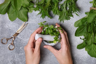 Woman grinding fresh green herbs in mortar at light grey table, top view