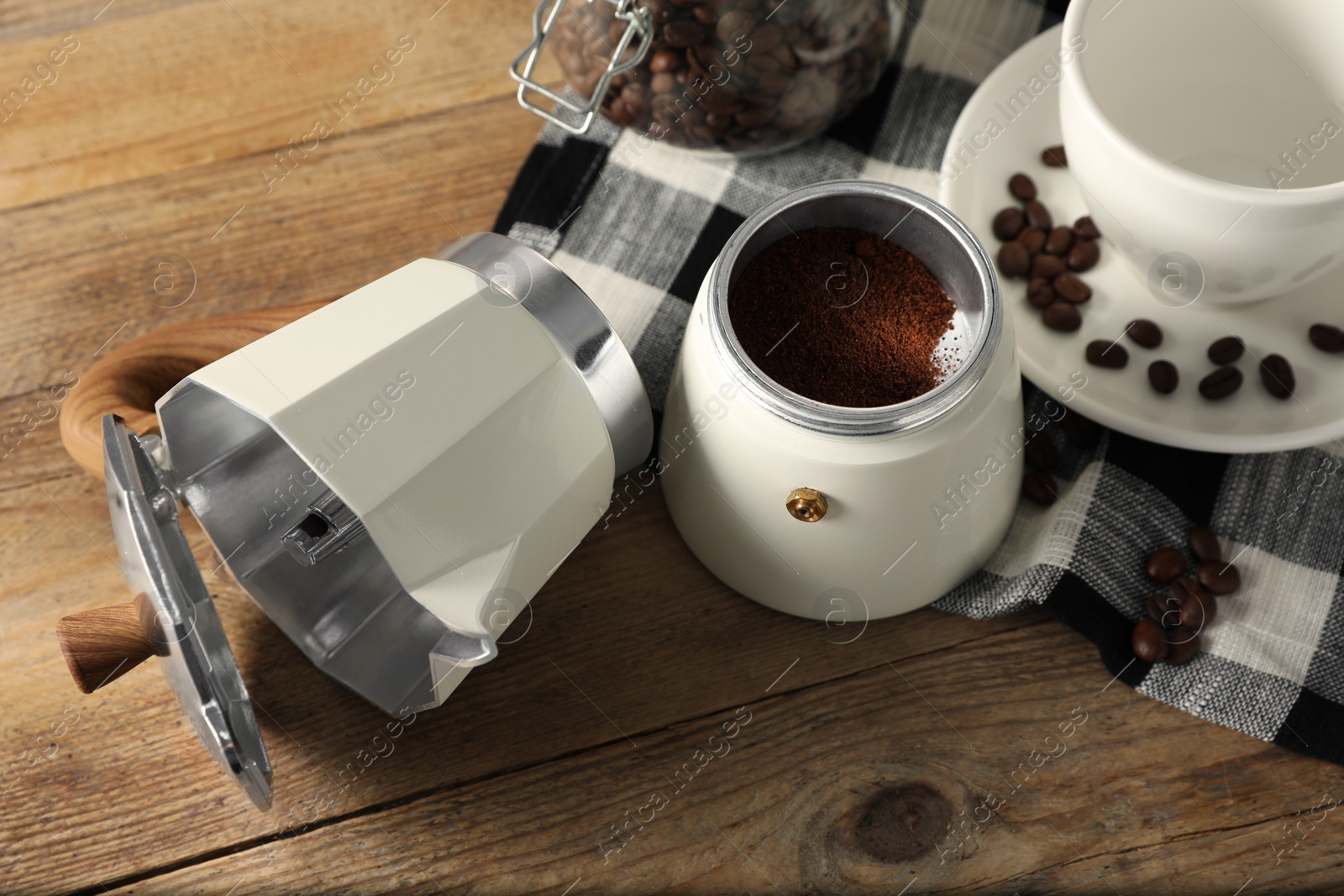 Photo of Moka pot with ground coffee, beans and cup on wooden table, above view