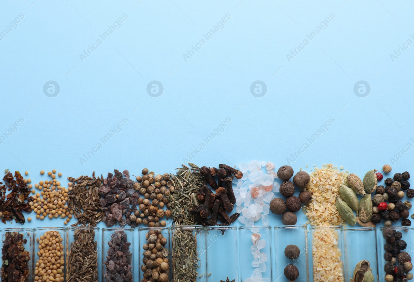 Photo of Glass tubes with different spices on light blue background, flat lay. Space for text