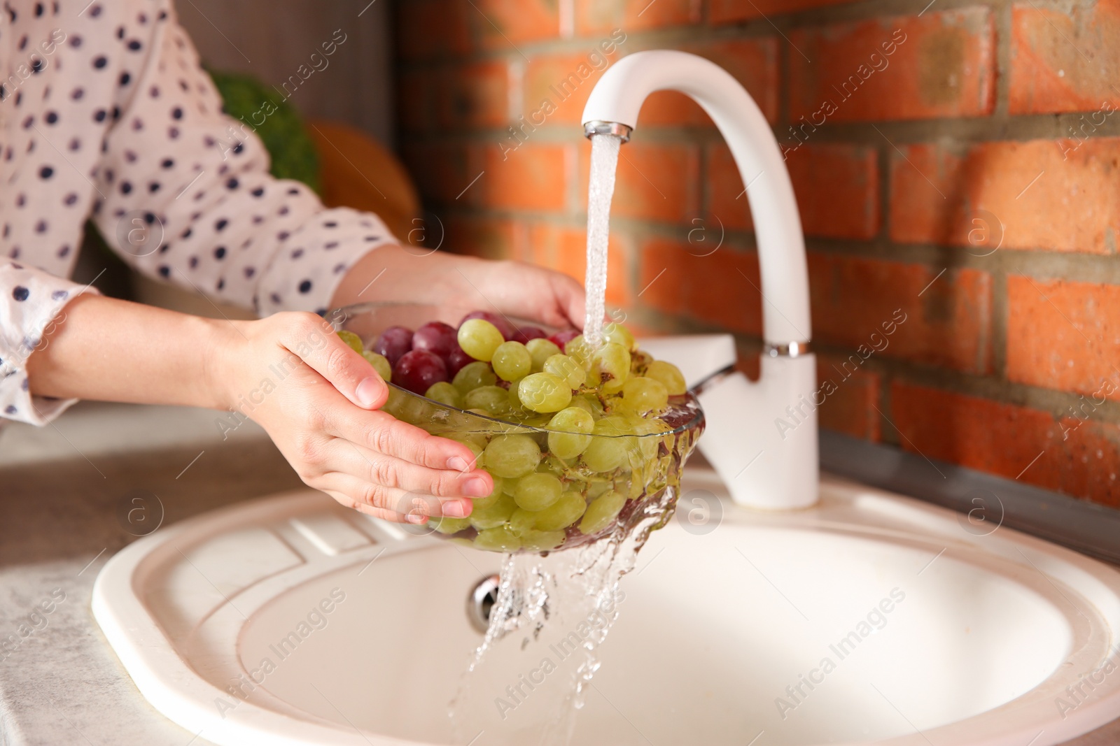 Photo of Woman washing fresh grapes in kitchen sink, closeup