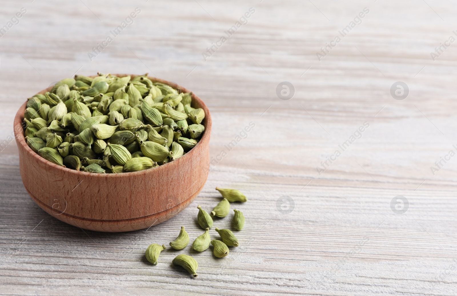Photo of Bowl with dry cardamom pods on wooden table. Space for text