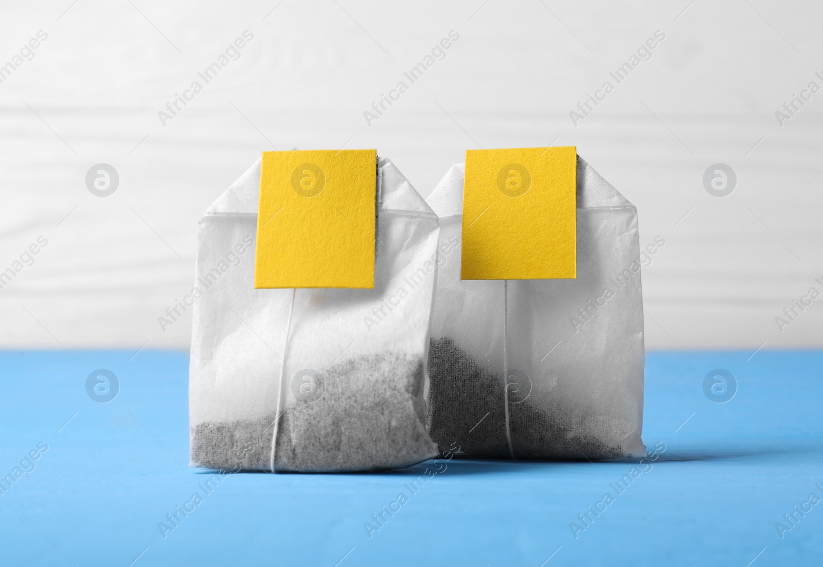 Photo of Tea bags with tabs on light blue wooden table, closeup