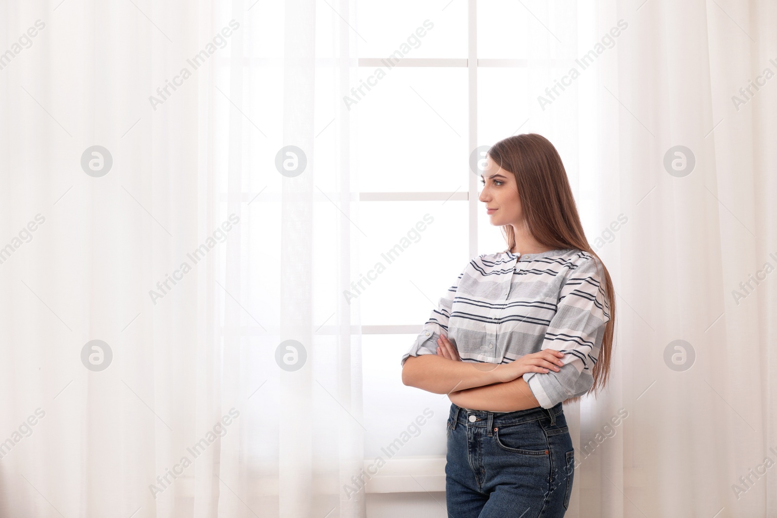 Photo of Young woman near window with open curtains at home. Space for text