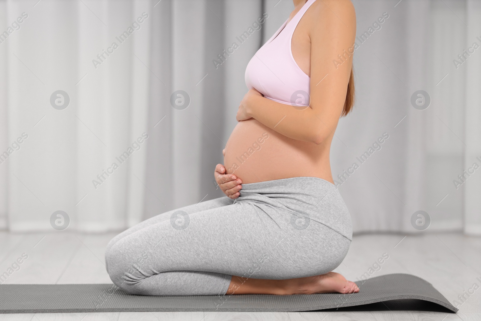 Photo of Pregnant woman sitting on yoga mat at home, closeup