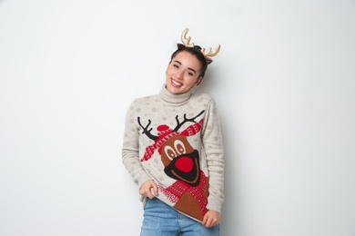 Photo of Young woman in Christmas sweater and deer headband on white background