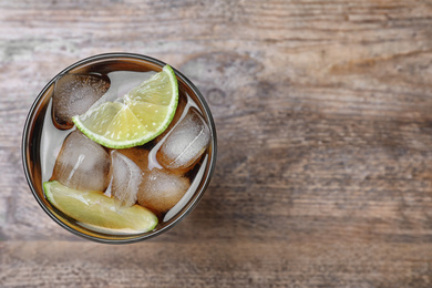 Photo of Glass of fresh Cuba Libre cocktail on wooden table, top view. Space for text