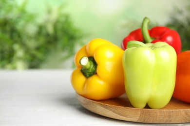 Photo of Wooden cutting board with ripe bell peppers on table against blurred background, closeup. Space for text