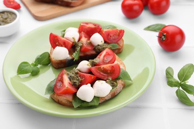 Delicious Caprese sandwiches with mozzarella, tomatoes, basil and pesto sauce on white tiled table, closeup