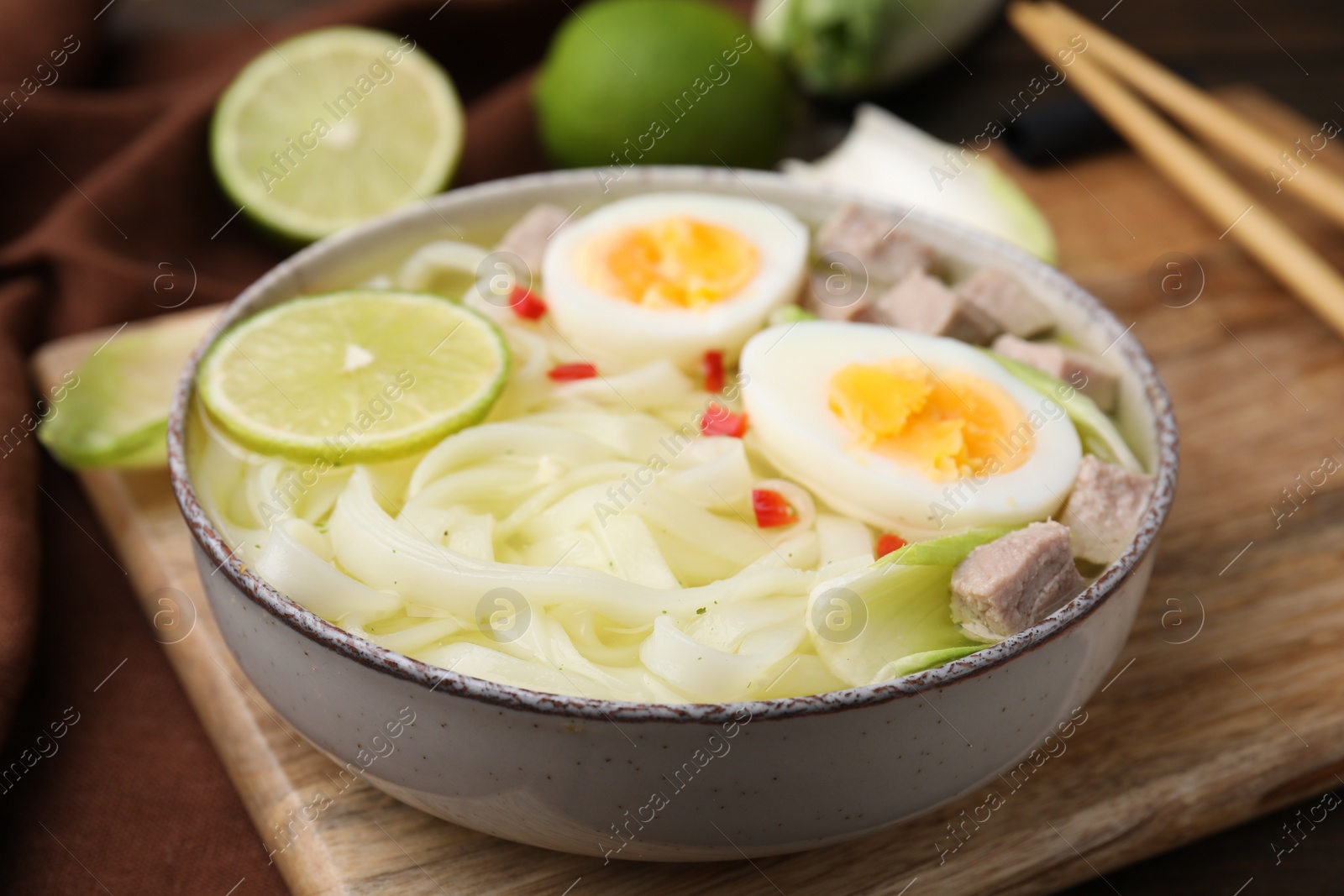 Photo of Bowl of delicious rice noodle soup with meat and egg on wooden board, closeup