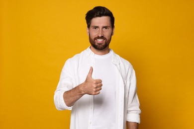 Photo of Handsome bearded man showing thumb up on orange background. Space for text