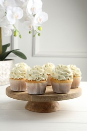 Tasty vanilla cupcakes with cream on white wooden table