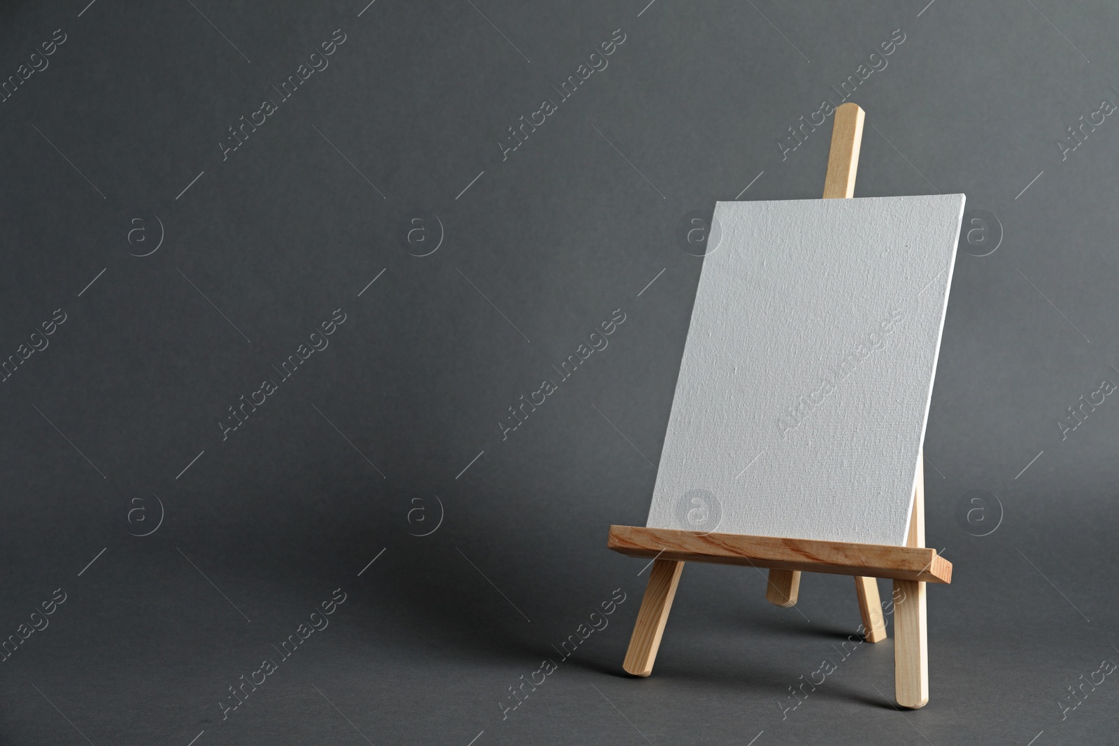 Photo of Wooden easel with blank canvas board on dark background, space for text. Children's painting