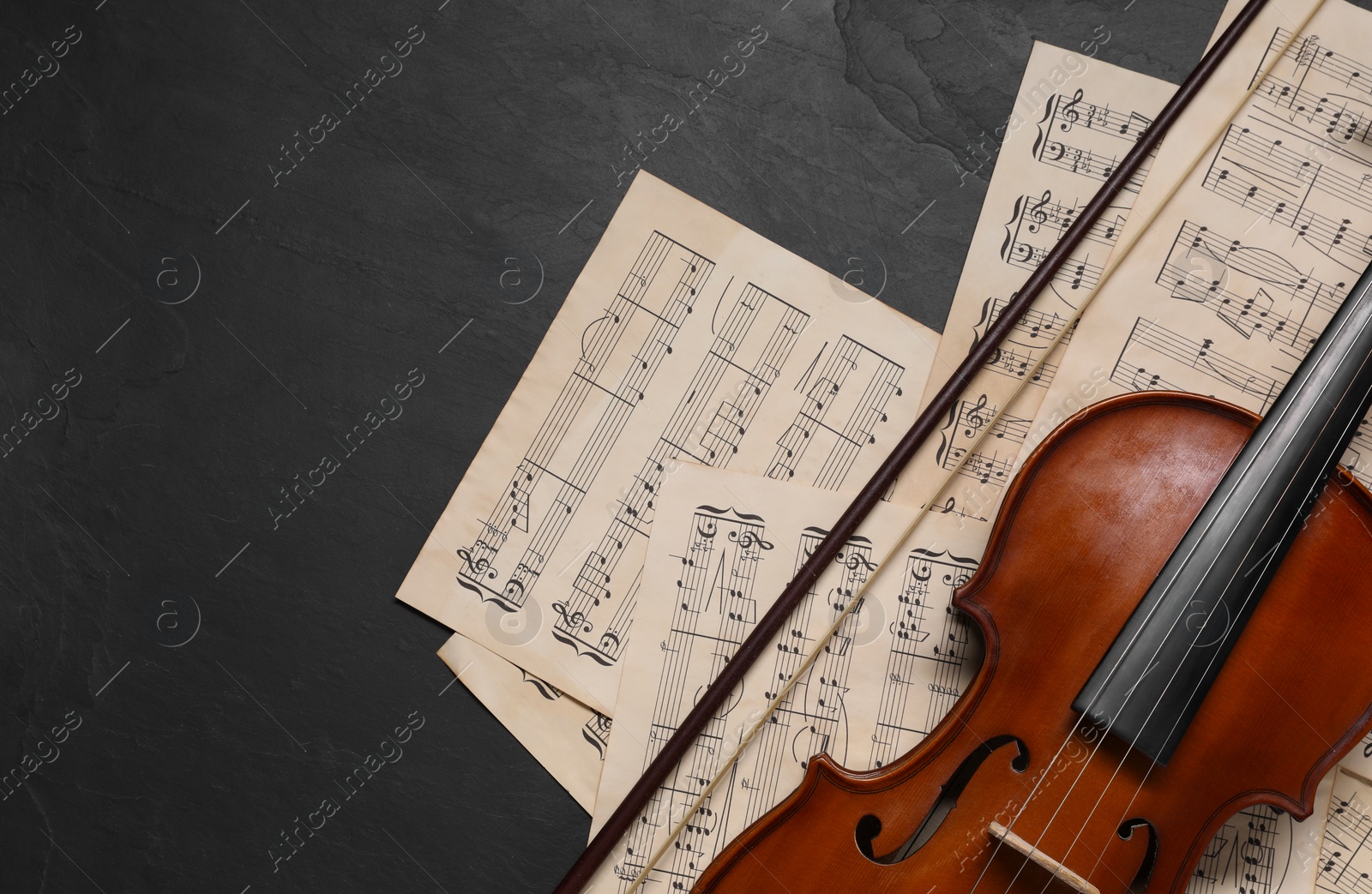 Photo of Violin, bow and music sheets on black table, top view. Space for text