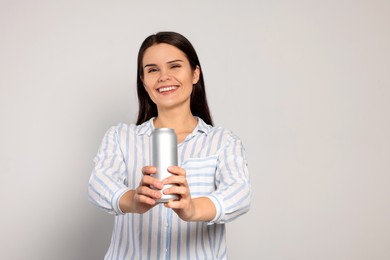 Beautiful young woman holding tin can with beverage on light grey background