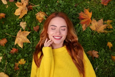 Photo of Smiling woman lying on grass among autumn leaves, top view