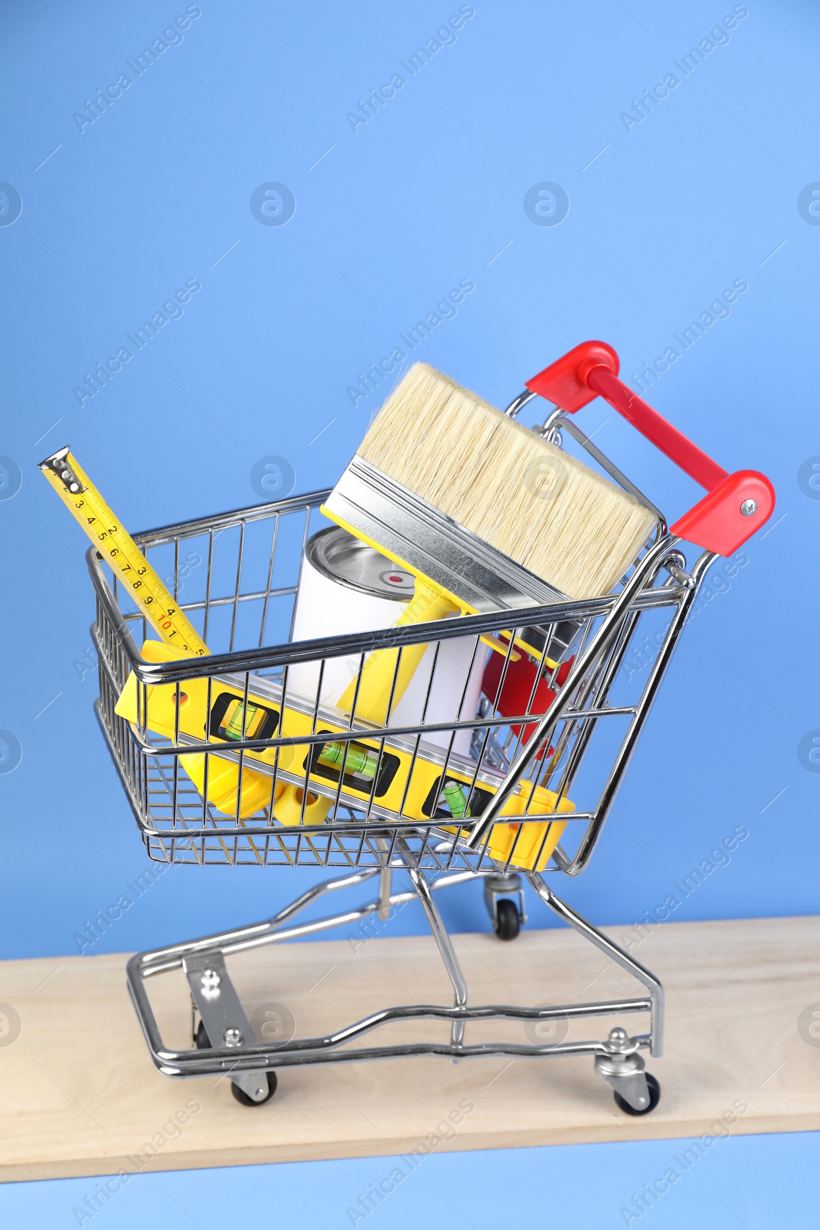 Photo of Small shopping cart with paint and renovation equipment on light blue background