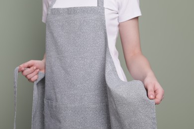 Photo of Woman putting on grey apron against light green background, closeup