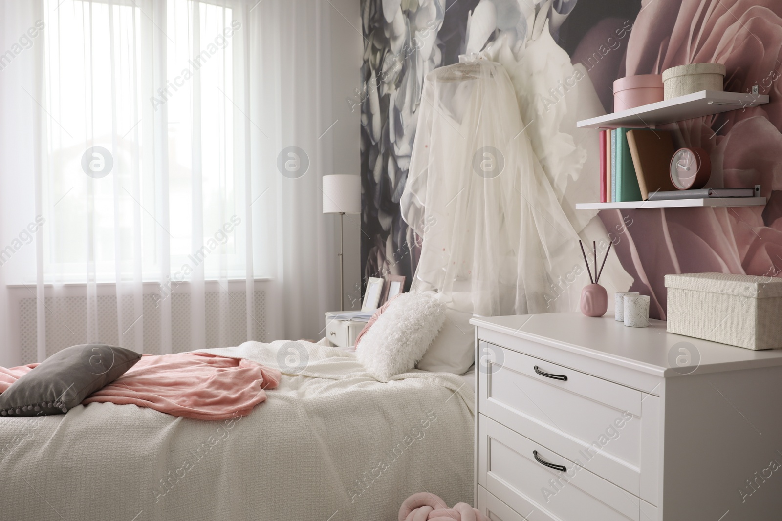 Photo of Teenage girl's room interior with comfortable bed, chest of drawers and floral wallpaper. Idea for stylish design