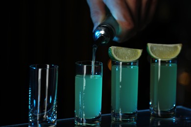 Photo of Bartender pouring alcohol drink into shot glass on dark background, closeup