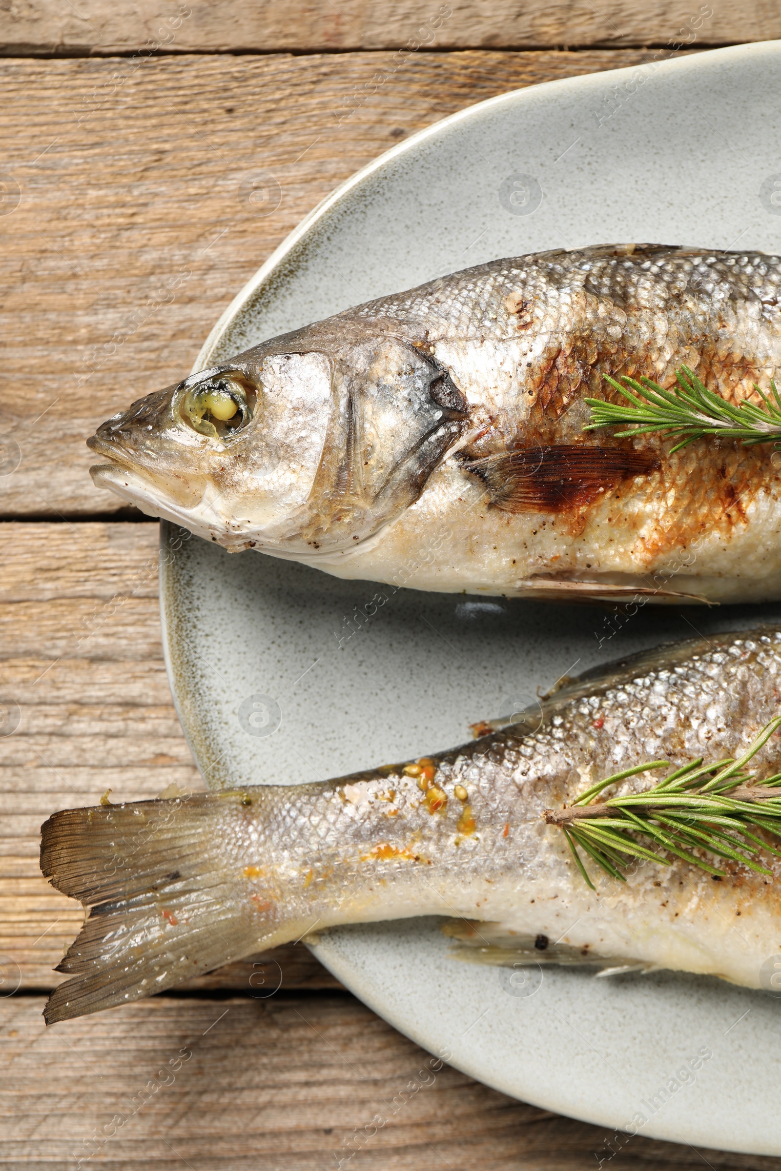 Photo of Delicious baked fish and rosemary on wooden table, top view