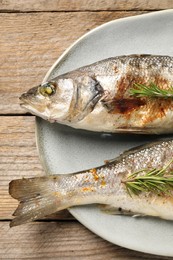 Photo of Delicious baked fish and rosemary on wooden table, top view