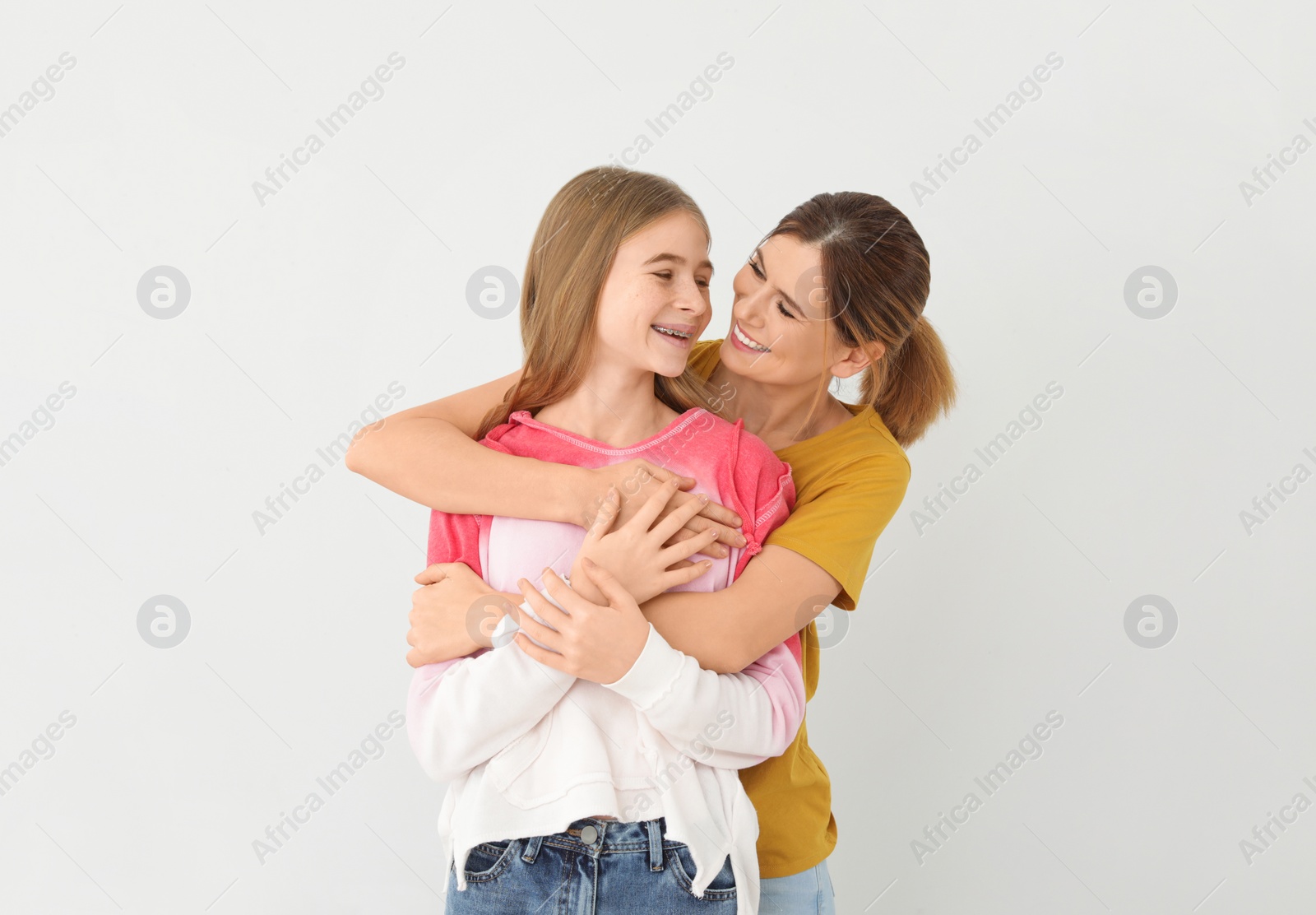 Photo of Happy mother hugging her teenager daughter on light background