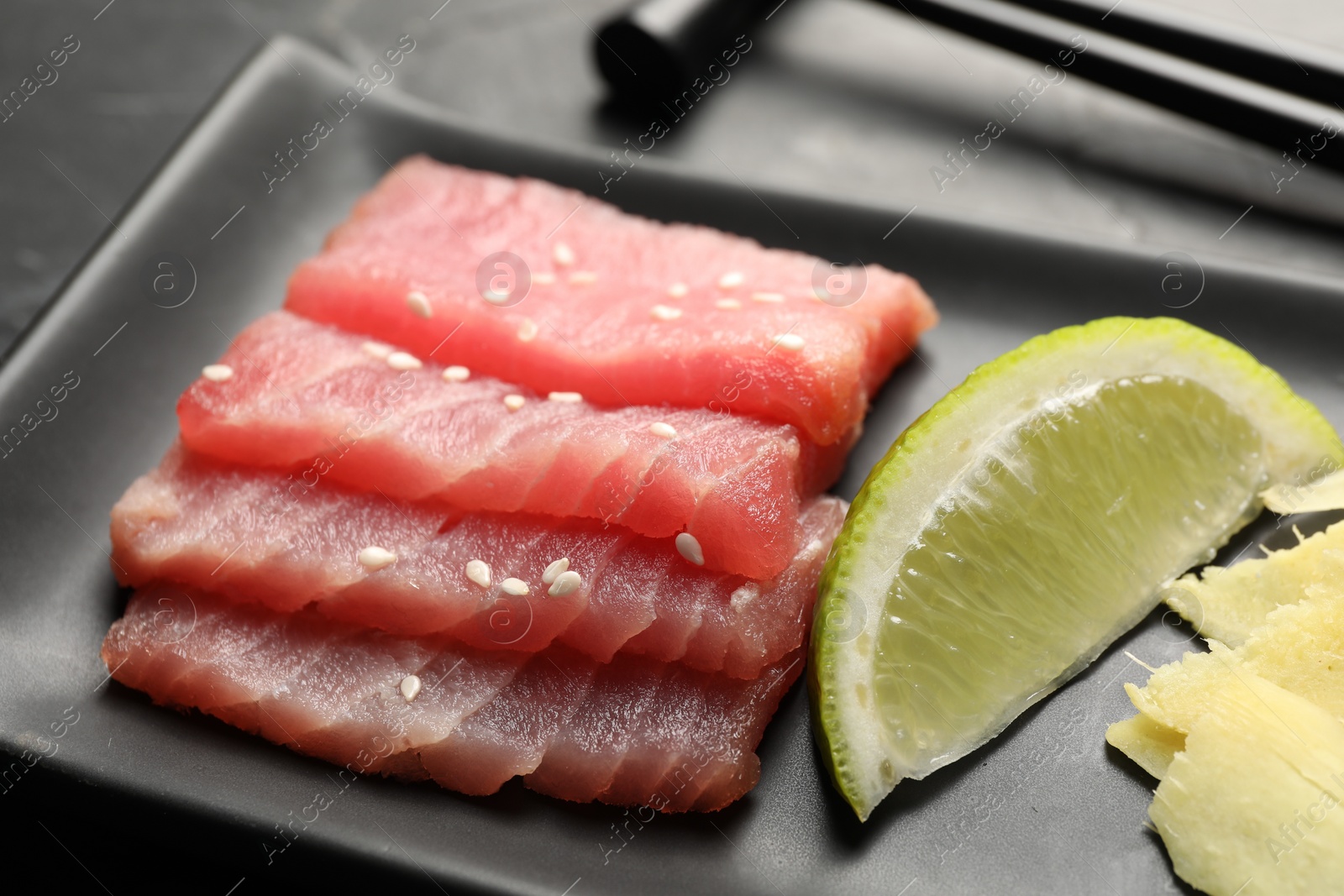 Photo of Tasty sashimi (pieces of fresh raw tuna) and lime wedge on black plate, closeup