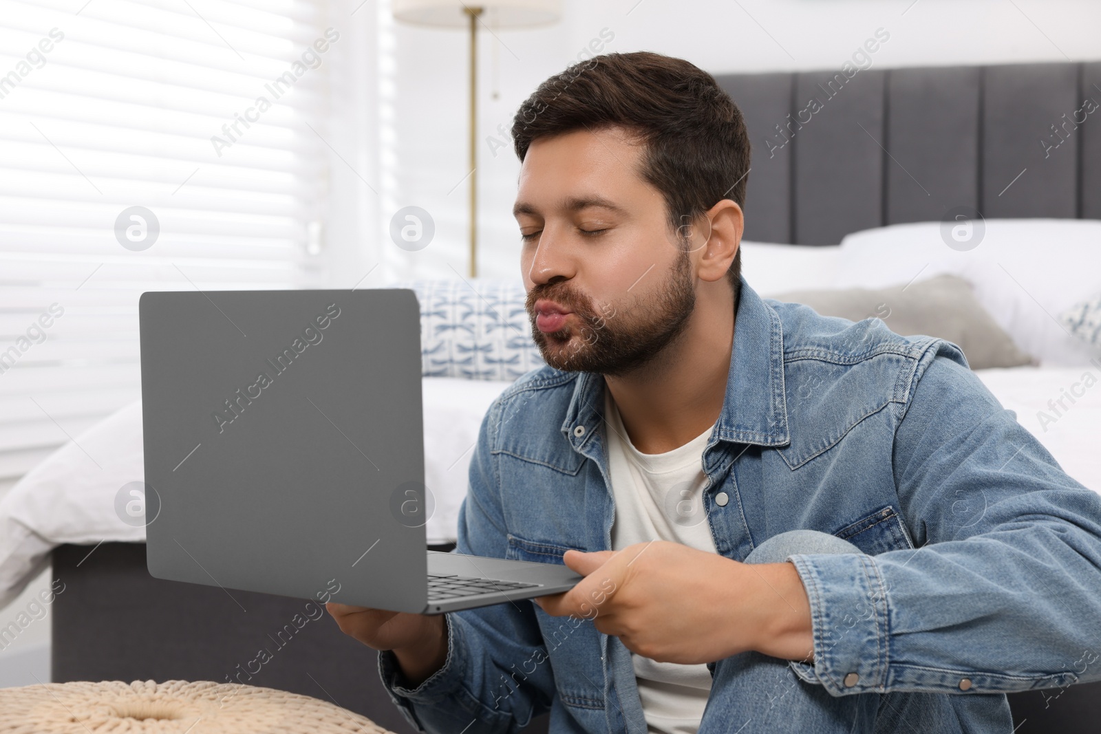 Photo of Man sending air kiss during video chat via laptop at home. Long-distance relationship