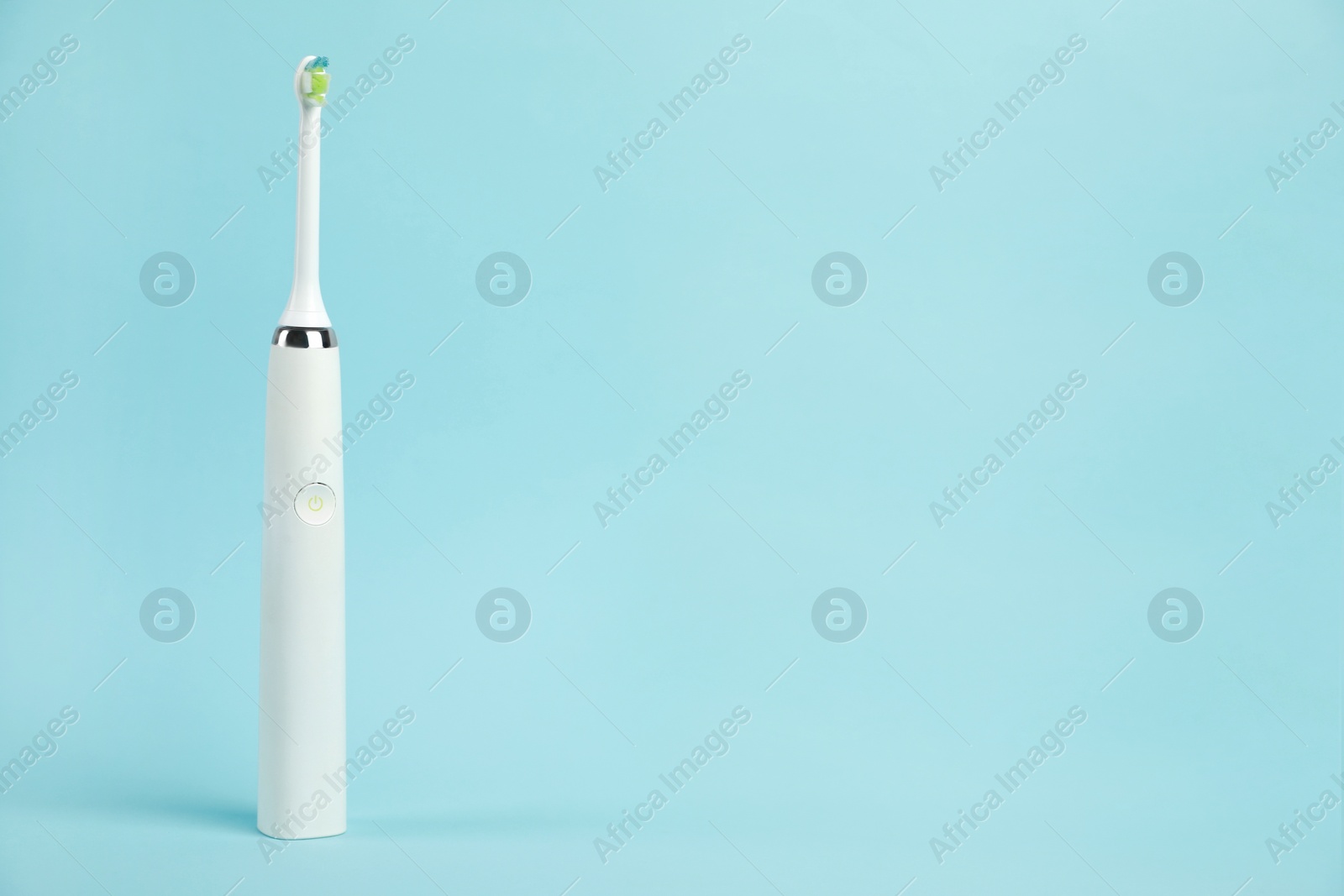 Photo of Electric toothbrush on light blue background, space for text