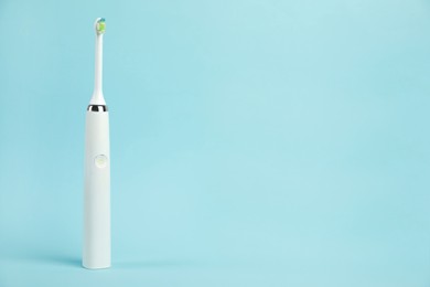 Electric toothbrush on light blue background, space for text