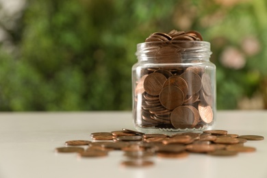 Photo of Donation jar with coins on table against blurred background. Space for text