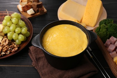 Photo of Fondue pot with melted cheese and different products on black wooden table