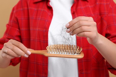 Woman untangling her lost hair from brush on beige background, closeup. Alopecia problem