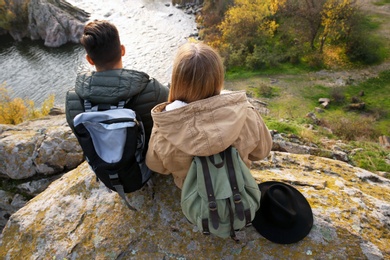 Photo of Couple of hikers with travel backpacks sitting on steep cliff, back view