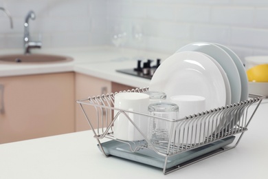 Photo of Dish drainer with clean dinnerware on table in kitchen. Space for text