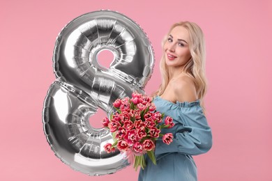 Photo of Happy Women's Day. Charming lady holding bouquet of beautiful flowers and balloon in shape of number 8 on pink background