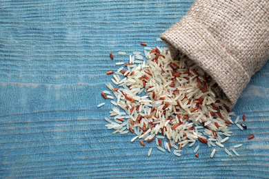 Photo of Mix of brown and polished rice in bag on blue wooden table, top view