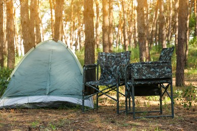 Camouflage chairs near camping tent in forest on sunny day