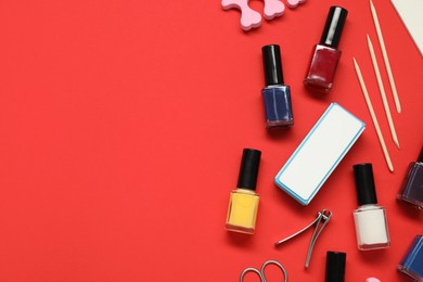 Photo of Nail polishes and set of pedicure tools on red background, flat lay. Space for text