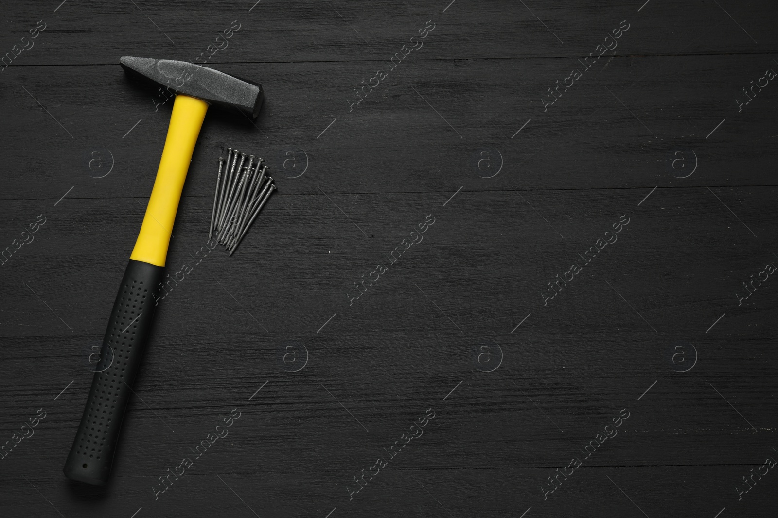 Photo of New hammer and metal nails on black wooden table, flat lay. Space for text