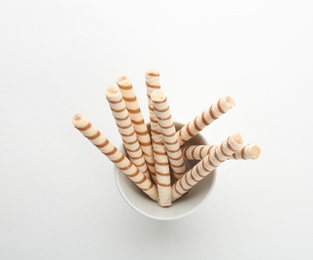 Bowl with tasty wafer roll sticks on white background, top view. Crispy food