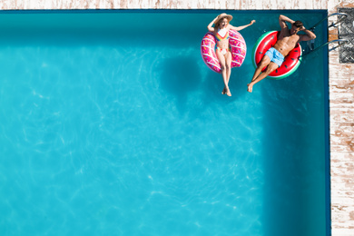 Happy couple with inflatable rings in swimming pool, top view and space for text. Summer vacation