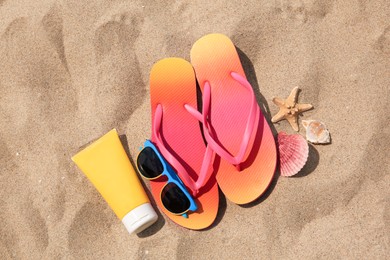 Photo of Flip flops and other beach accessories on sand, flat lay