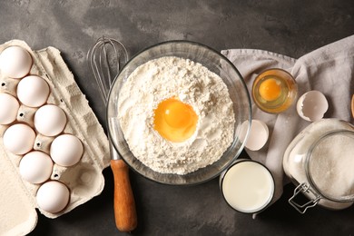 Making dough. Flour with egg yolk in bowl and other products on grey textured table, flat lay